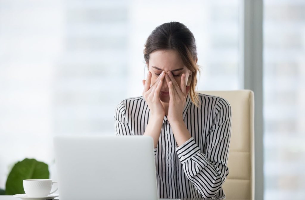 A woman experiencing dry eye syndrome rubbing both of her eyes.