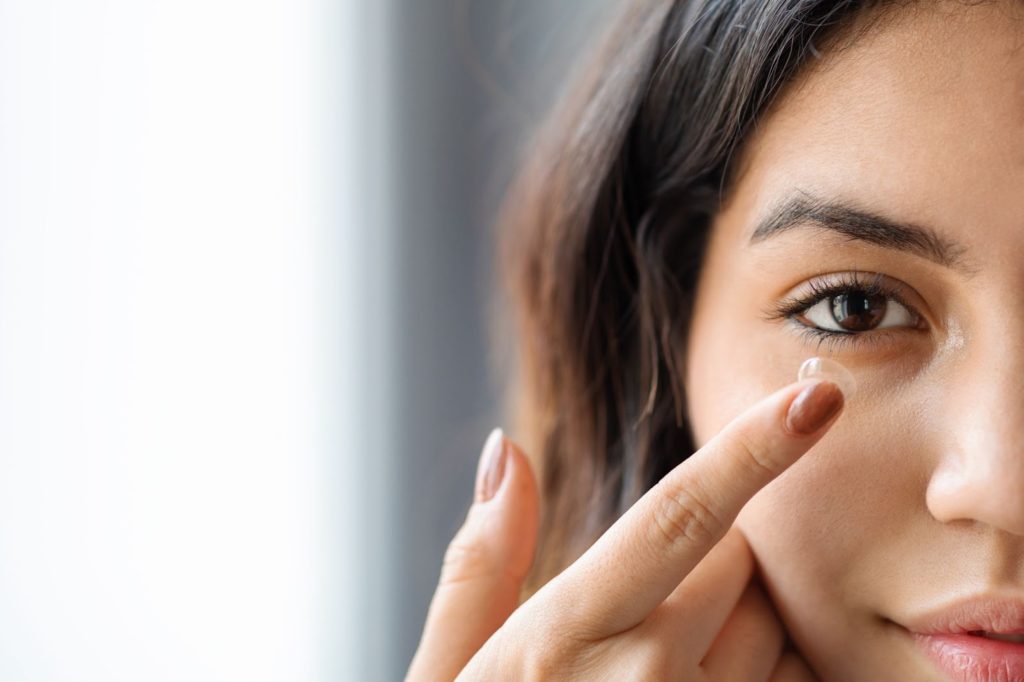 A closeup of a young woman placing a contact lens in her eye.