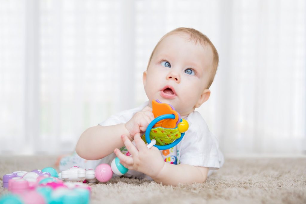 A baby with crossed eyes playing with a toy on a carpet.