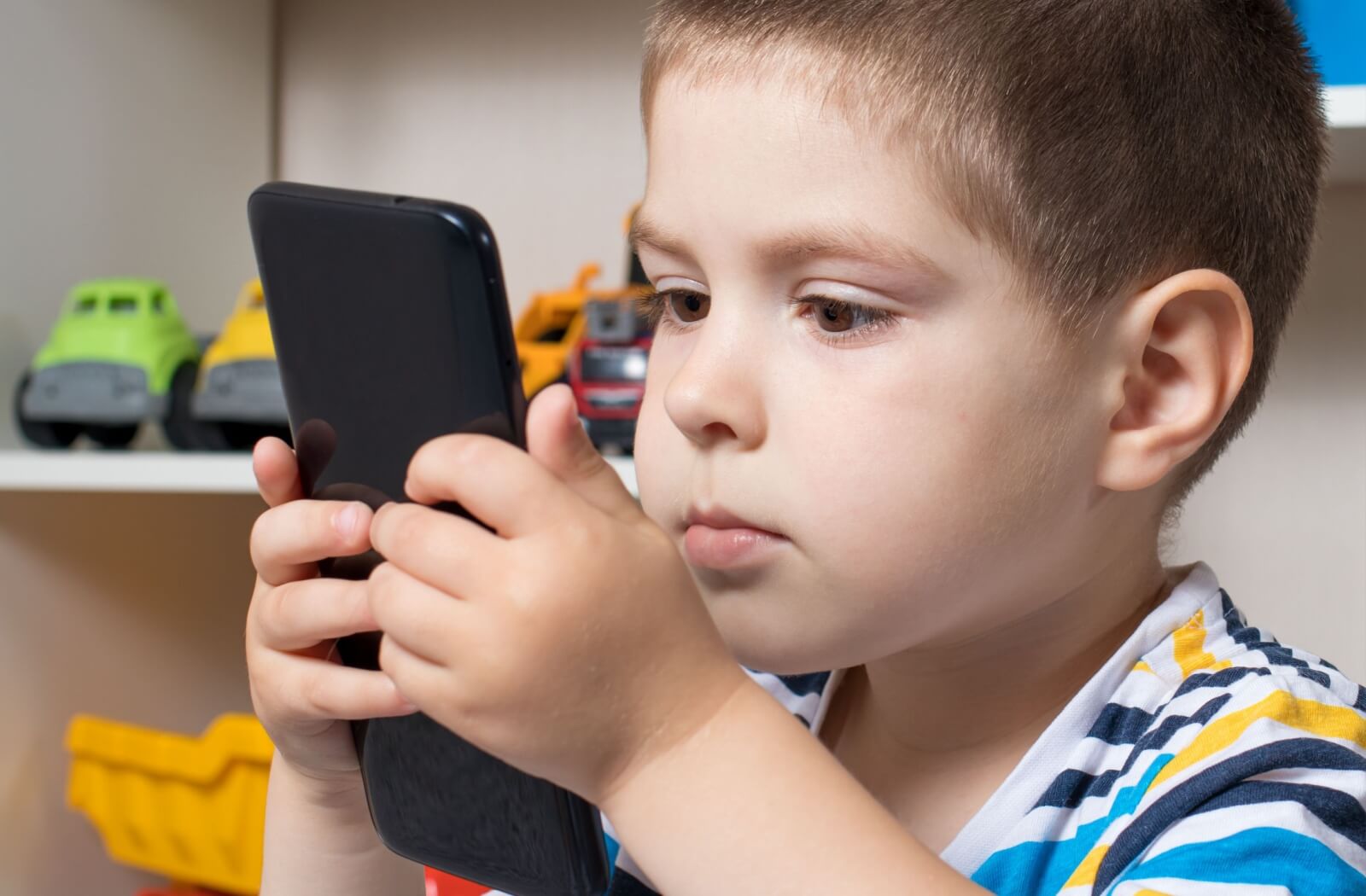 A young boy holds his phone close to his face, indicating that he could be developing myopia and may be a candidate for MiYOSMART lenses.