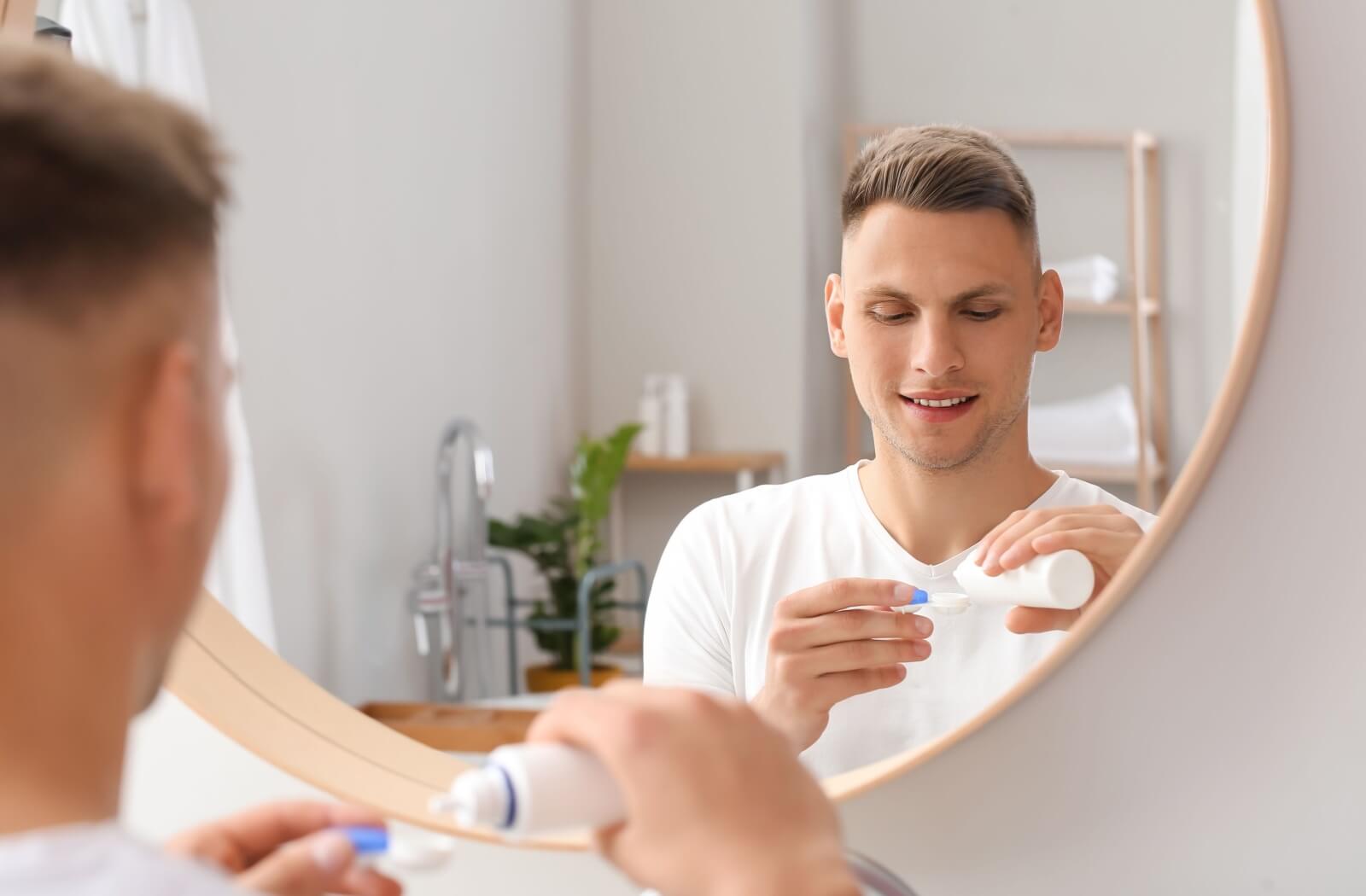 A person standing in front of a bathroom mirror using contact lens solution to clean their contact lenses.