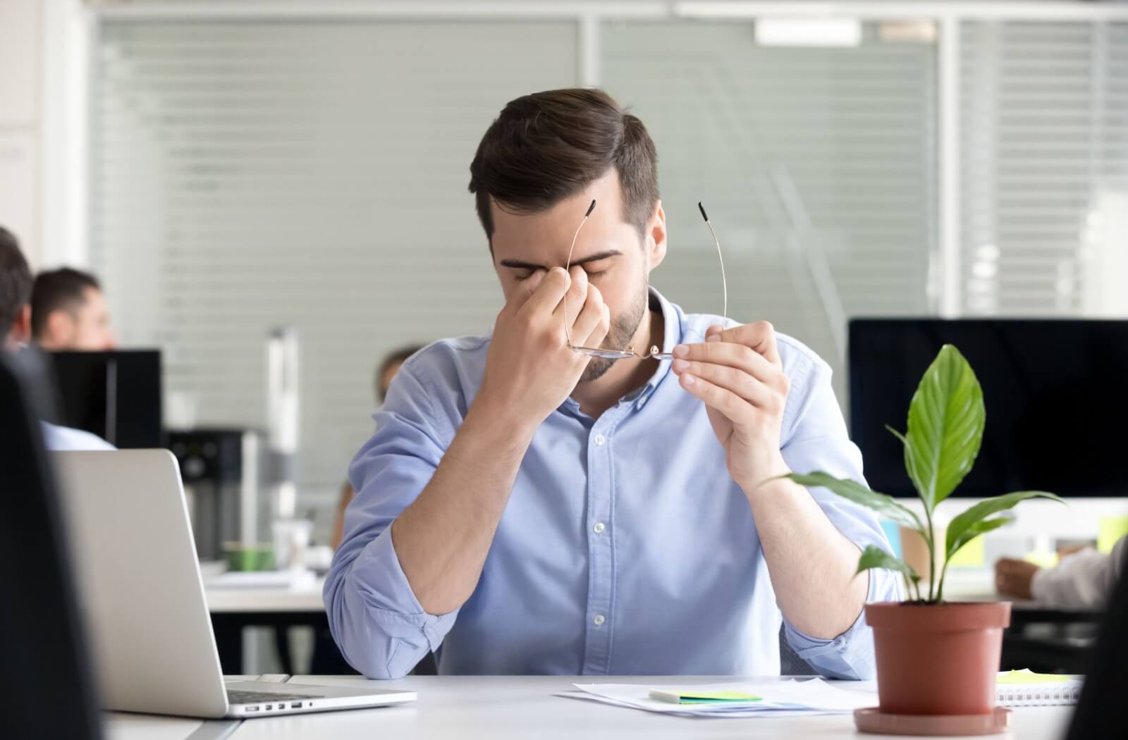 A young professional in their office taking off their glasses to rub their eyes due to eye strain.