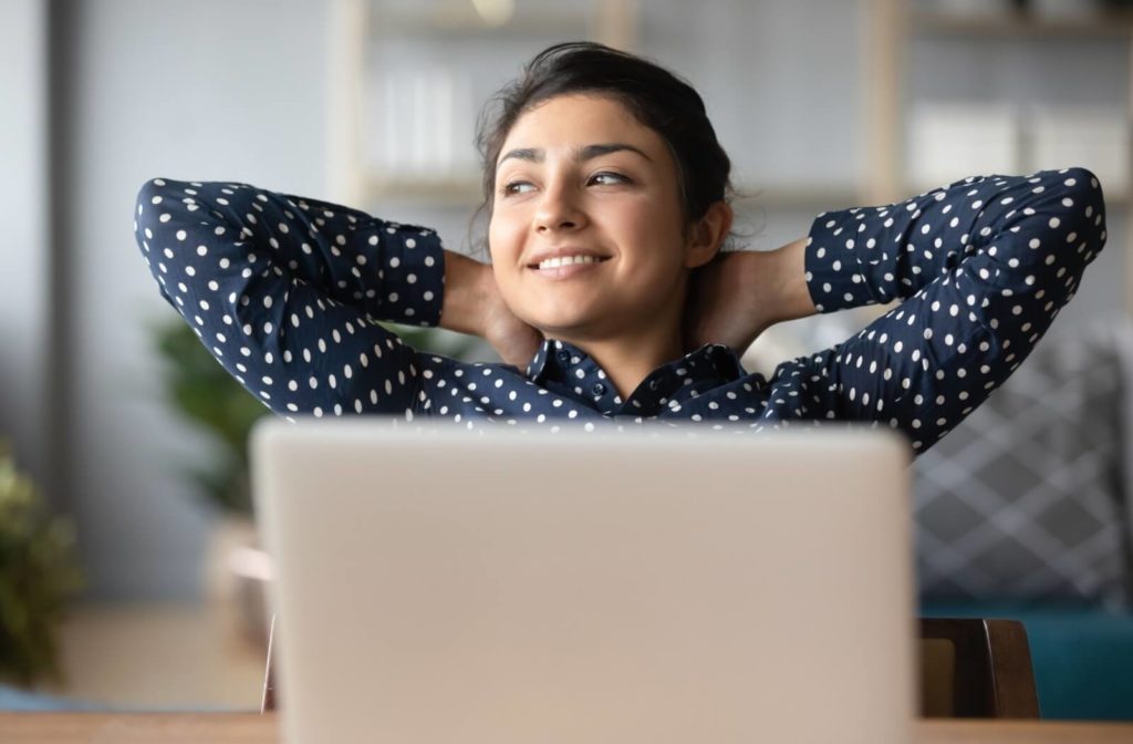 A young adult resting with their hands behind their head while working at their laptop to prevent eye strain.